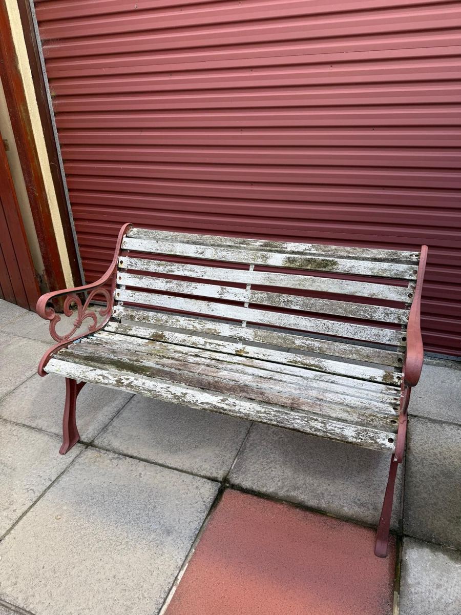 Garden bench with peeling white slats and faded red cast iron ends