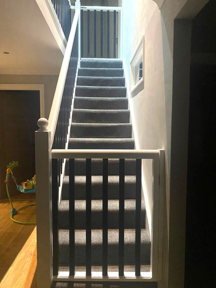 Bespoke gate at the bottom of a carpeted staircase, white frame with black spindles